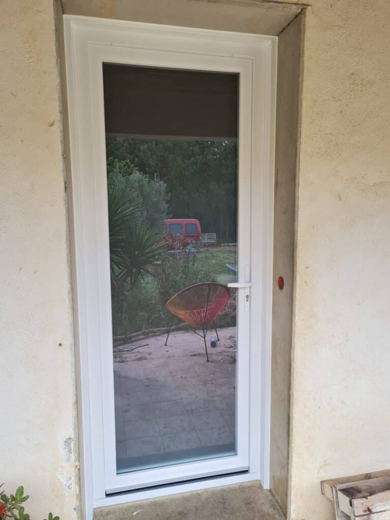 Nouvelle porte-fenêtre PVC blanche fraîchement installée donnant sur une terrasse carrelée et un jardin verdoyant avec une voiture rouge.